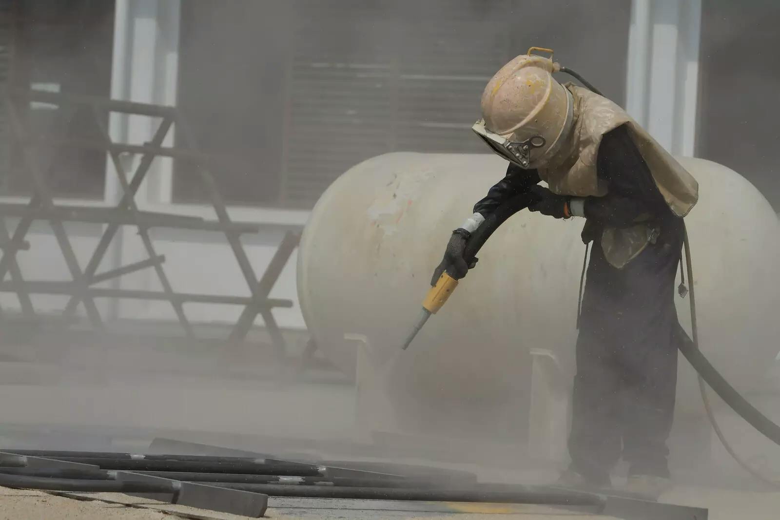 A worker sandblasting a metal structure